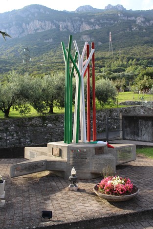 Monumento ai caduti partigiani, con colonne di metallo colorate in bianco, rosso e verde, immerso nel verde.
