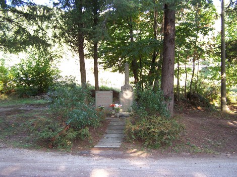 Cippo di San Quirico, memoriale immerso nella natura, circondato da alberi e fiori, luogo di meditazione e ricordo.