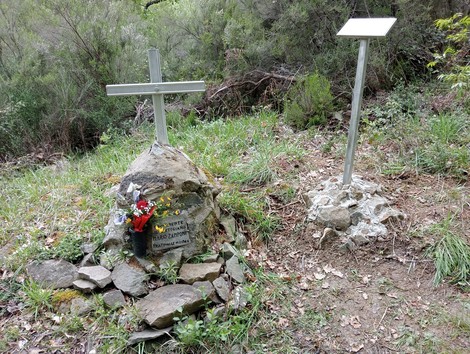 Cippo commemorativo a Zamponi, con fiori e croce, immerso nella natura. Sentiero verde circostante.
