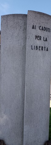 Monumento ai caduti per la Libertà, struttura in pietra con incisioni commemorative. Ambiente all'aperto.