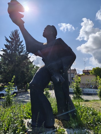 Monumento al Partigiano, statua in bronzo con figura eretta che tiene un cappello, immersa nel verde.