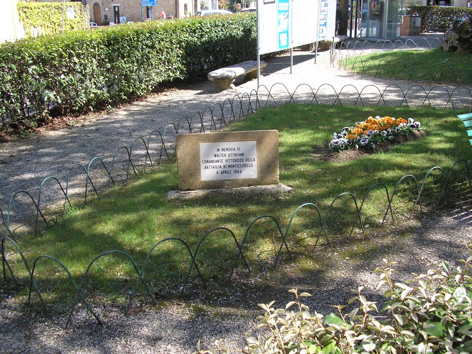 Cippo commemorativo dedicato a Ottaviani, situato in un giardino curato con aiuole fiorite.