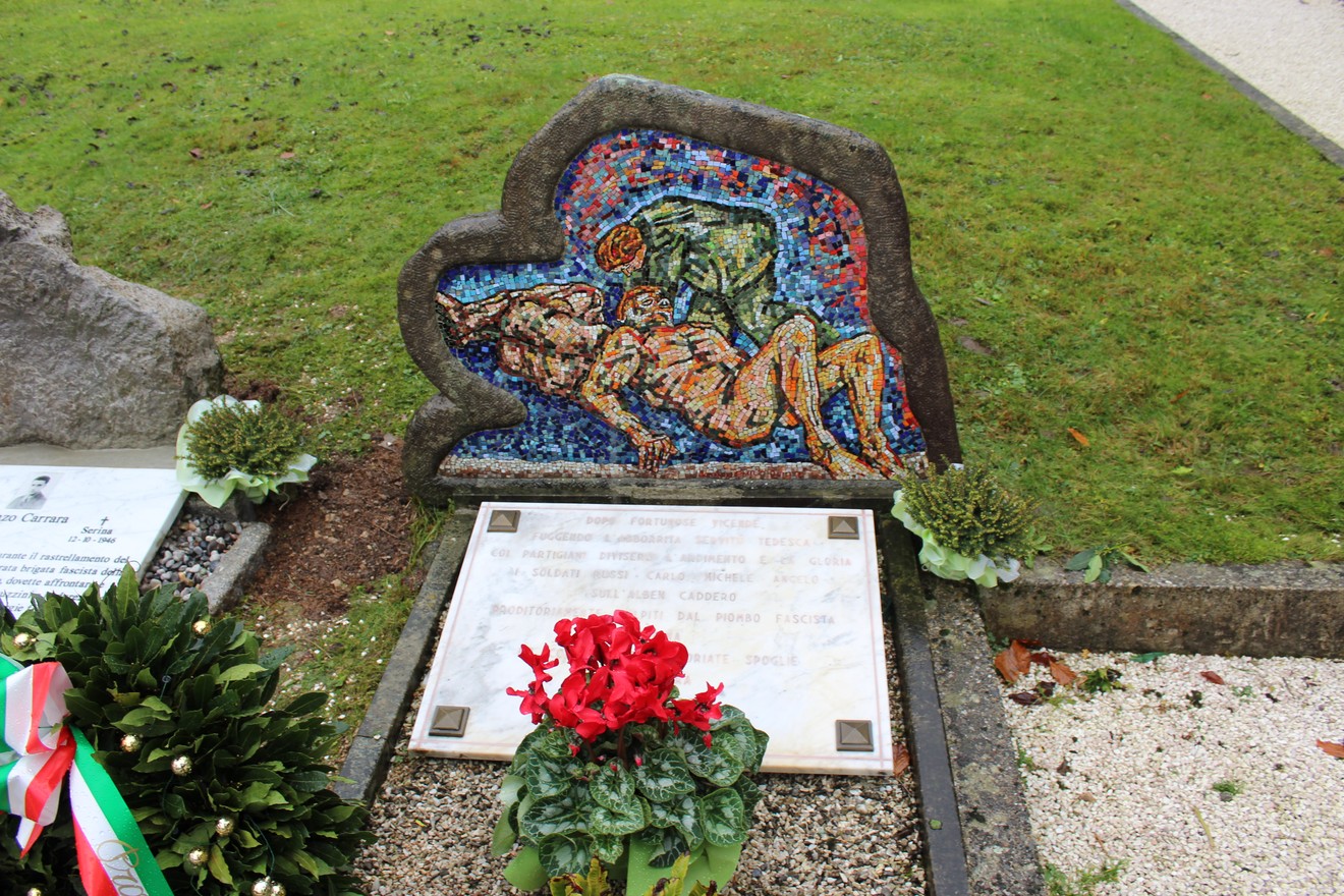 Monumento ai caduti partigiani russi, con mosaico e dedica commemorativa in un contesto verde curato.