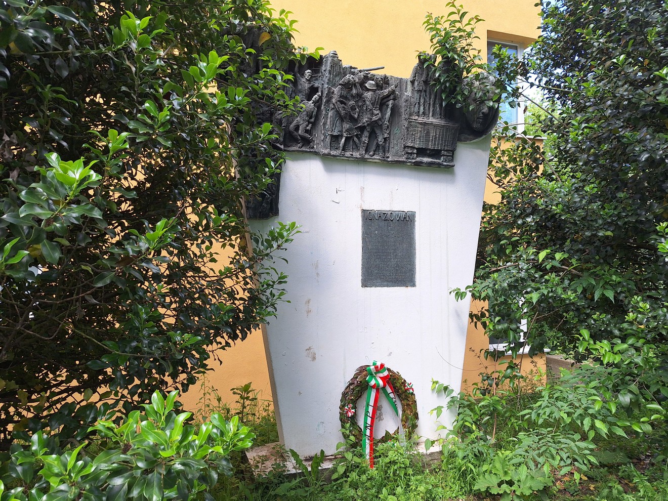Monumento a Vian circondato da vegetazione, con una corona tricolore ai piedi della struttura.