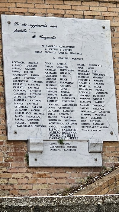Monumento commemorativo ai caduti, con elenco di nomi incisi su una lapide in una struttura di mattoni.