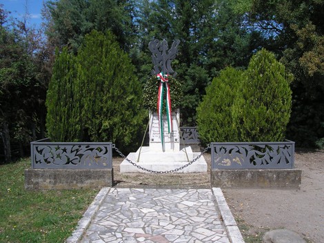 Monumento commemorativo a Ponte del Ricci, circondato da alberi e decorato con un nastro tricolore.