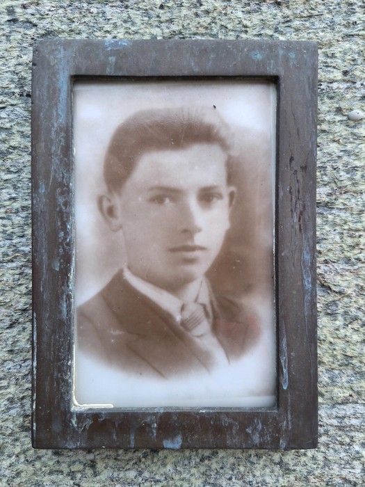 Ritratto in bianco e nero di un giovane uomo, incorniciato su una lapide in pietra.