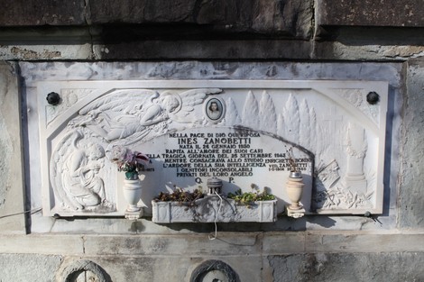 Targa commemorativa in memoria delle vittime dei bombardamenti con decorazioni floreali e simboli di ricordo.