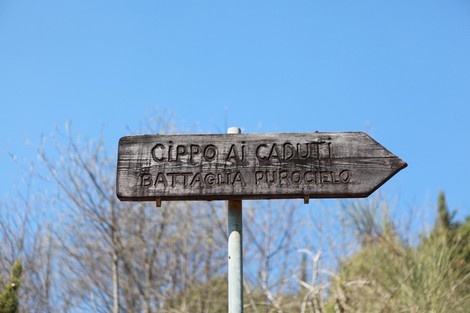 Indicazione segnaletica verso il "Cippo ai caduti" in memoria della battaglia di Purocielo, con sfondo blu del cielo.