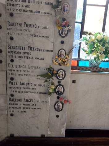 Lapide commemorativa con foto e nomi di caduti per la libertà, decorata con fiori, in un ambiente sobrio.