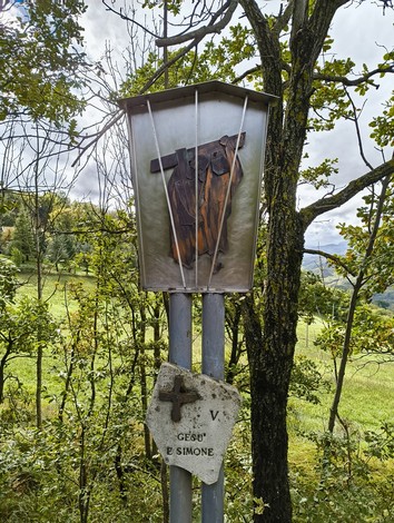Via Crucis di Casaglia, una croce su un supporto metallico in un contesto naturale con alberi e colline verdi.