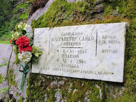Lapide commemorativa di Carlo Balzaretti, intitolata a un valoroso combattente, adornata con fiori.