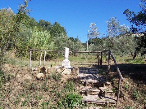 Cippo del podere di Grancaia, monumento in un paesaggio verdeggiante con ulivi e cereali.