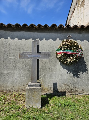 Croce a Gerelli accanto a una corona di alloro, su sfondo di un muro grigio e cielo blu.