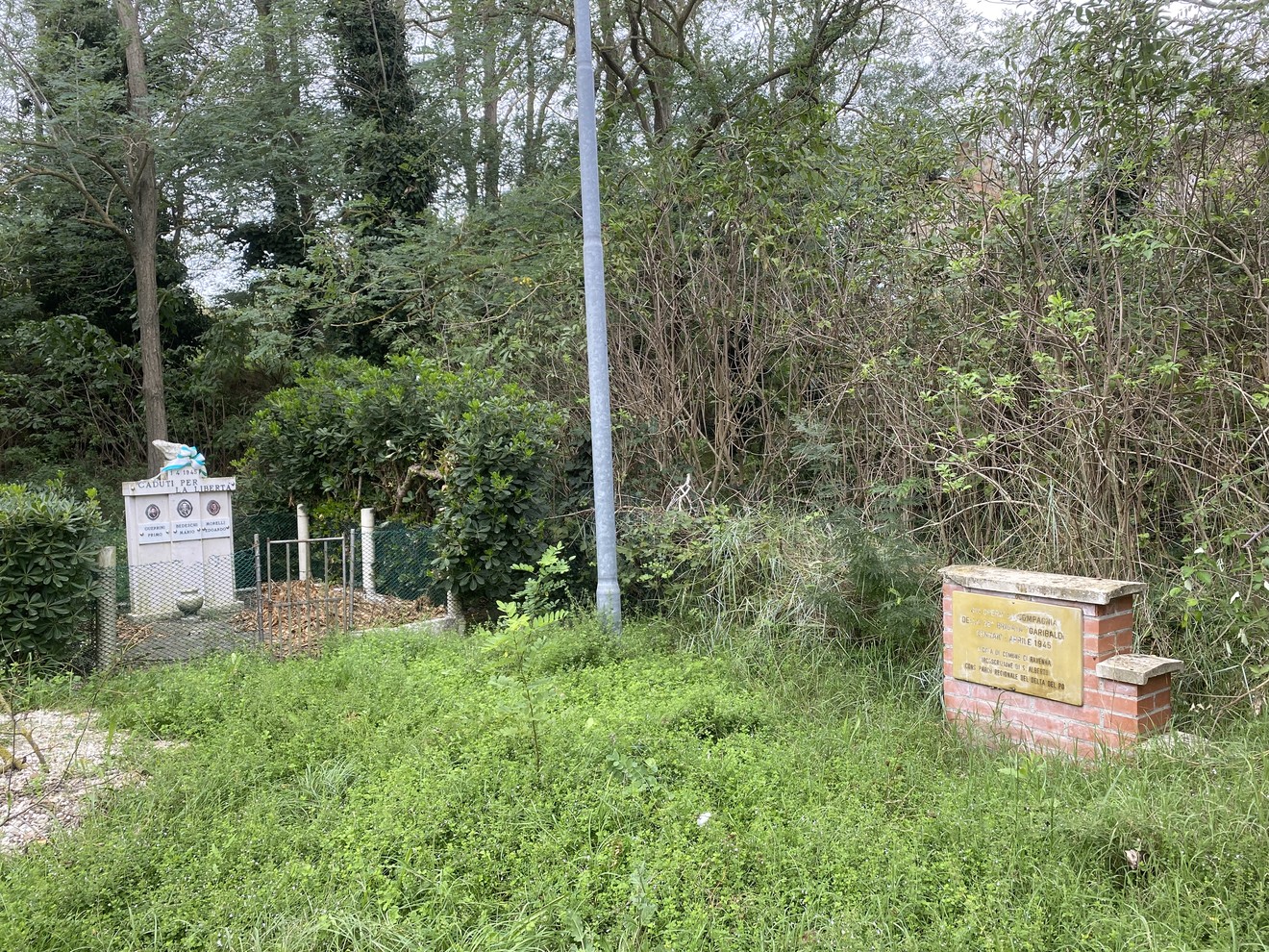 Monumento a Guerrini, Bedeschi e Morelli immerso nella vegetazione, con un'area recintata e segnaletica.