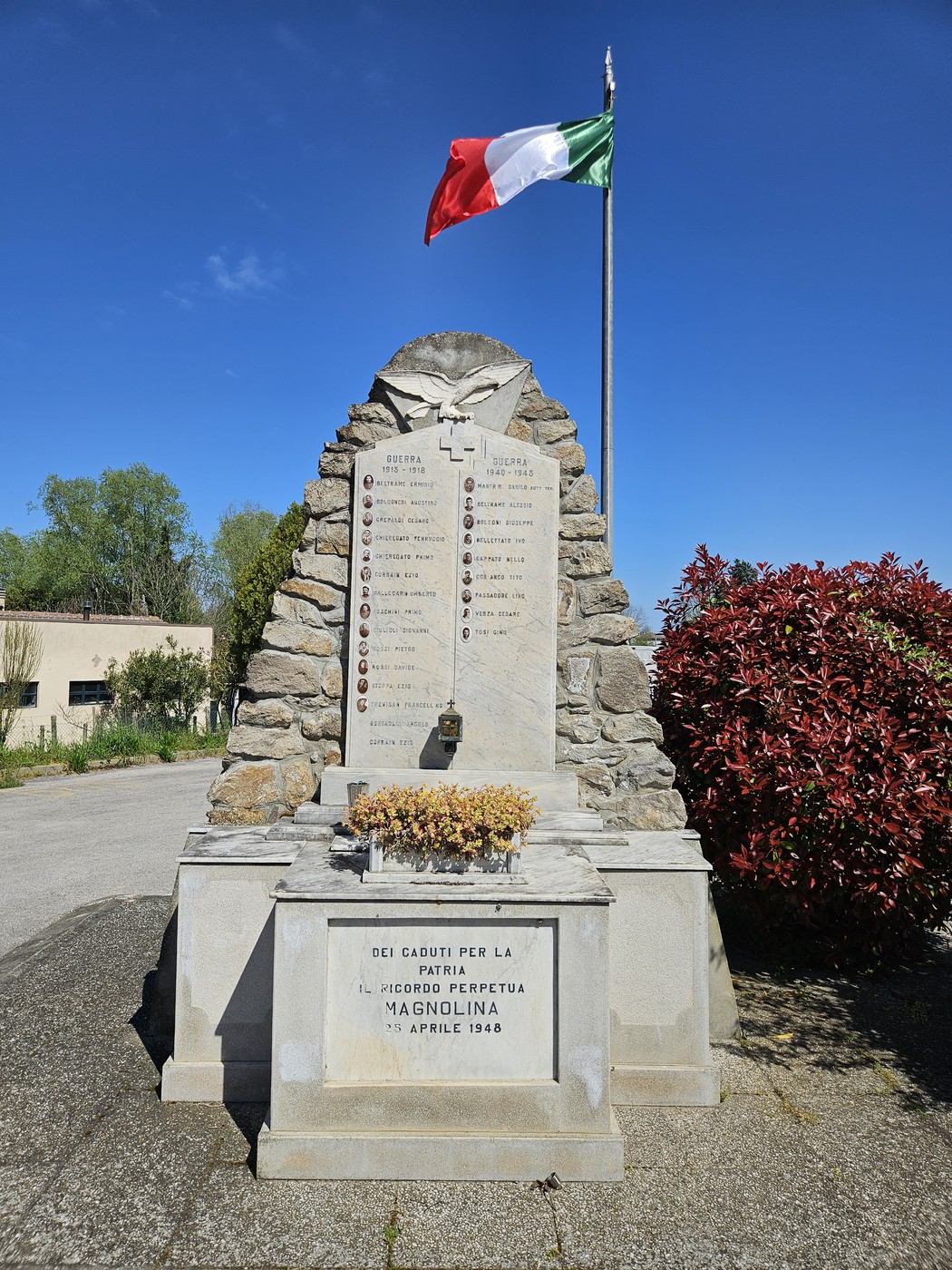 Monumento ai Caduti di Magnolina, con una stele commemorativa e il tricolore italiano che sventola sullo sfondo.