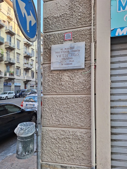 Lapide con iscrizione su parete d'angolo di un edificio, lungo una via cittadina.