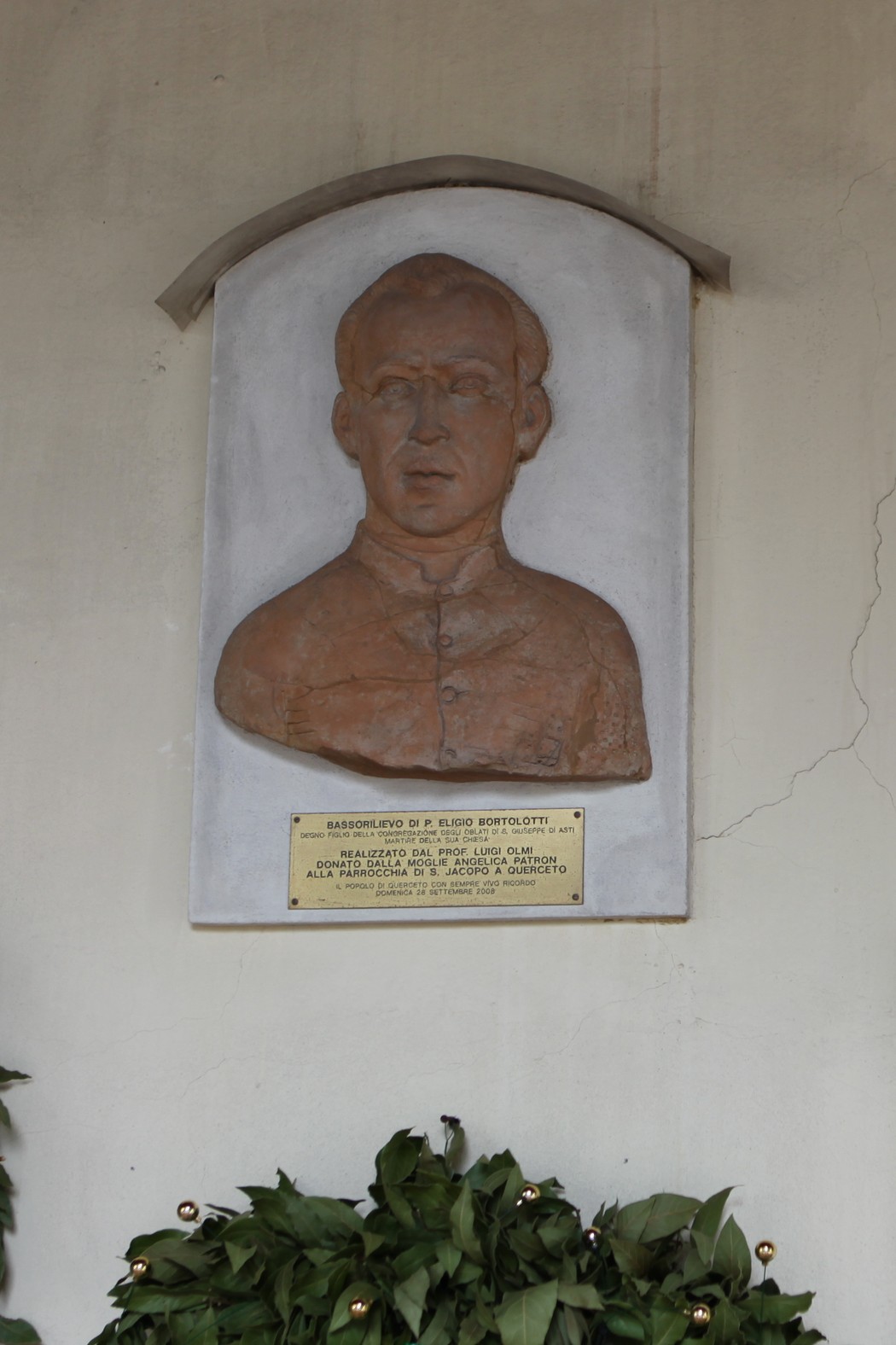 Bassorilievo dedicato a Don Bortolotti, con ritratto e placca commemorativa, situato in un contesto storico.