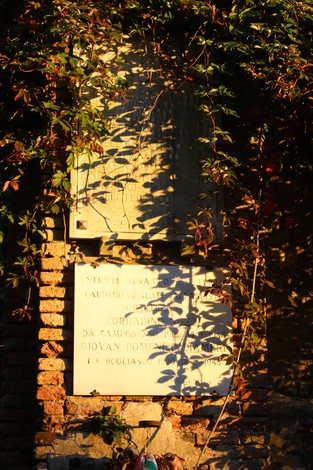 Lapide commemorativa ai partigiani fucilati al Forte Castellaccio, con vegetazione circostante e giochi di ombre.