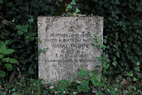 Cippo commemorativo dedicato a Giulio Valente, vittima del fascismo, situato in un'area verde.