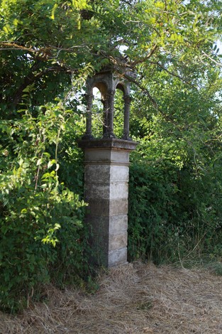 Cippo commemorativo ai caduti, circondato da vegetazione in un paesaggio naturale.