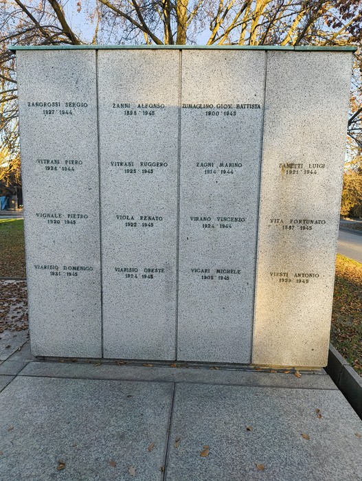 Monumento commemorativo con nomi incisi, dedicato ai caduti in guerra, circondato da alberi e natura.