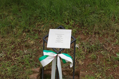 Cippo commemorativo con dedica, situato in un'area verde, circondato da erba.