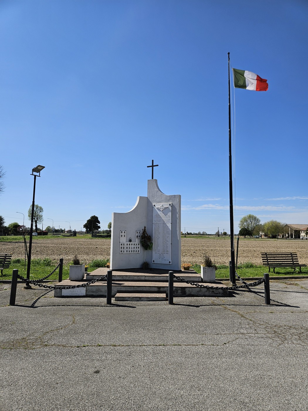 Monumento ai Caduti di Valliera con bandiera italiana, situato in un'area aperta e soleggiata.
