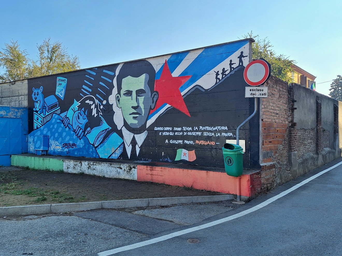 Murale su parete esterna con ritratto di un giovane, stella rossa e figure stilizzate, con iscrizione.