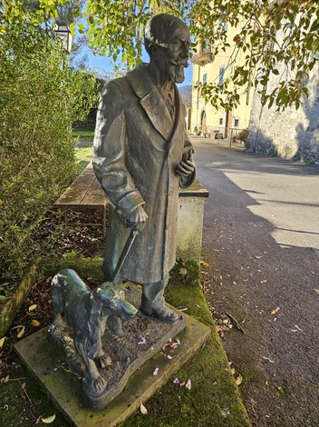 Monumento a Benedicenti, scultura di un uomo in soprabito con un cane, circondato da vegetazione.