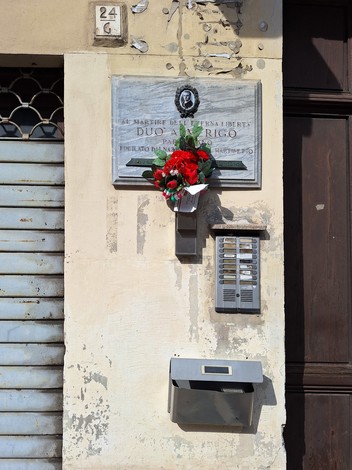 Lapide commemorativa di Duò, adornata con fiori, su una parete storica di un edificio.