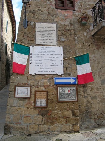 Lapide commemorativa per Mencatelli e Cappelli, con bandiere italiane e indicazioni stradali.