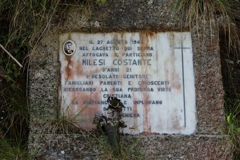 Lapide commemorativa dedicata a Milesi Costante, ubicata in un contesto naturale.