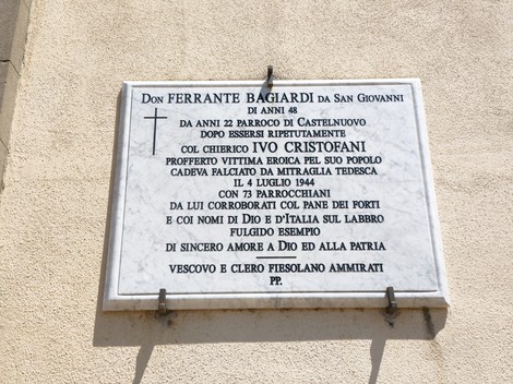 Lapide in marmo con iscrizione e croce incisa, fissata su una parete esterna intonacata.