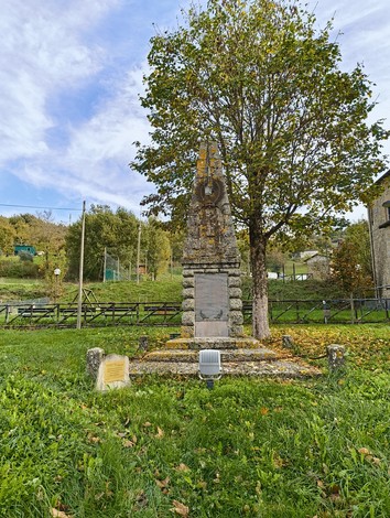 Cippo commemorativo dedicato all'accoglienza degli sfollati, immerso nel verde e circondato da alberi.