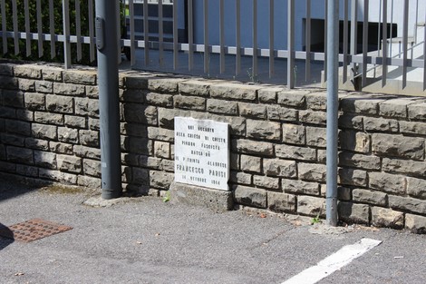 Lapide commemorativa di Francesco Parisi su una parete di pietra, situata in un'area urbana.