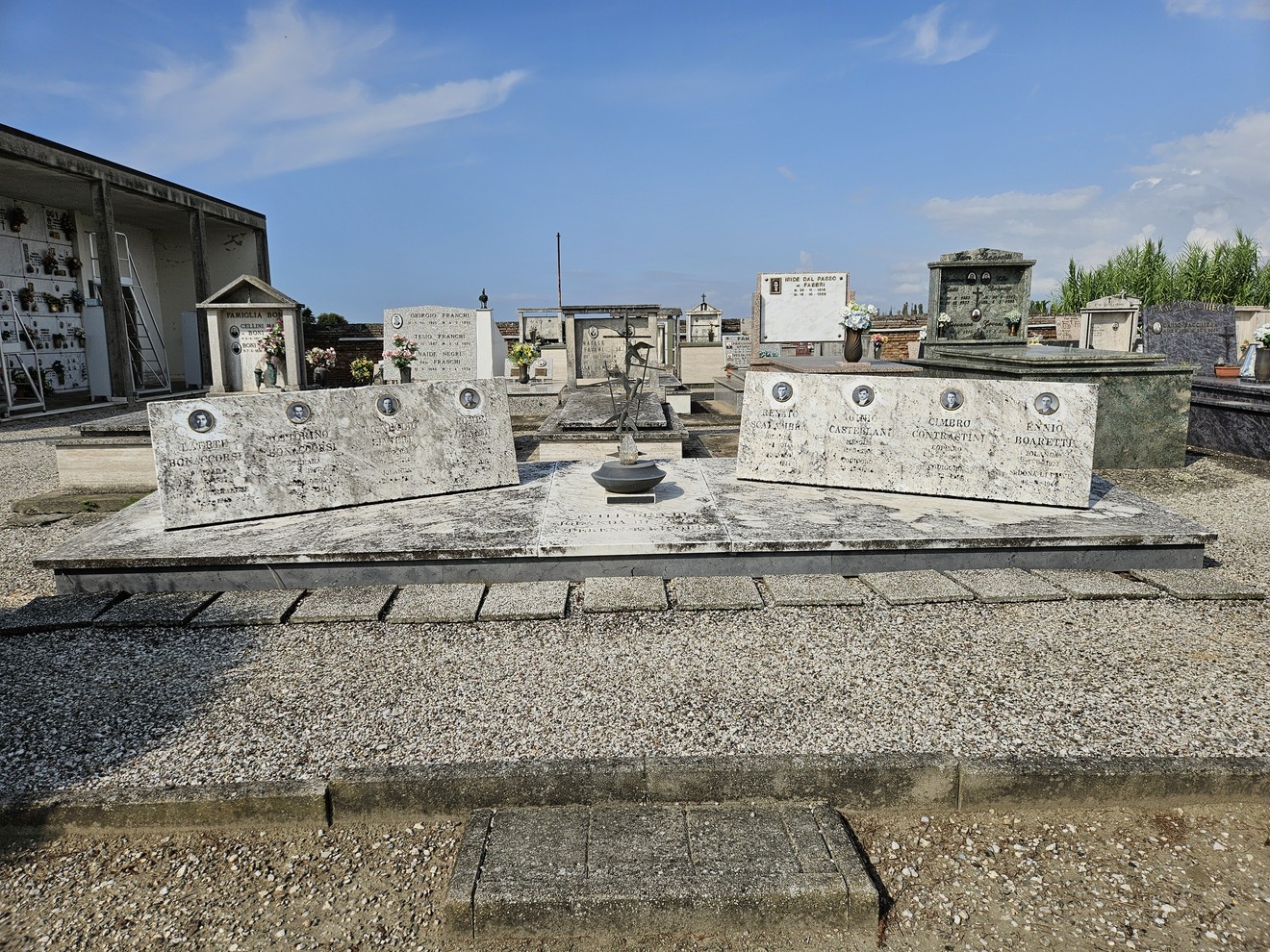 Sacrario dei Partigiani, monumento commemorativo con lapidi in un cimitero, sotto un cielo sereno.