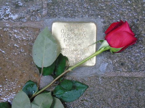 Pietra d'inciampo dedicata a Giuseppina Polacco con una rosa posata sopra, su pavimentazione di cobblestone.