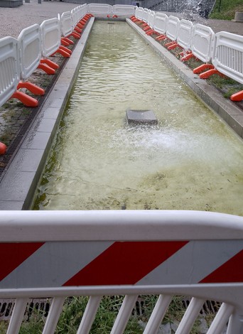 Monumento ai Partigiani, con una vasca d'acqua circondata da barriere di sicurezza e elementi decorativi.