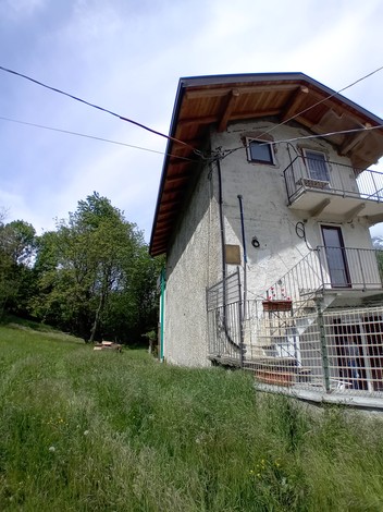 Edificio rustico in mezzo alla natura, con piante verdi e cielo nuvoloso sullo sfondo.