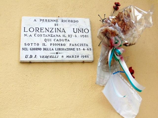 Lapide commemorativa in onore di Lorenza Unio, vittima del fascismo, con fiori e decorazioni.