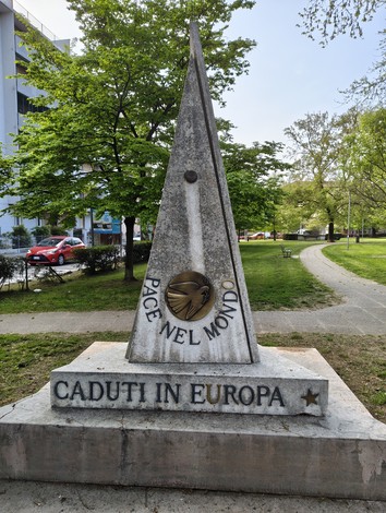 Monumento ai caduti con obelisco in marmo, incisi messaggi di pace e commemorazione in un parco.