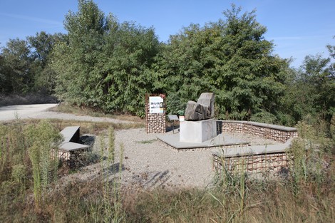 Monumento ai Martiri del Panaro circondato da una vegetazione verde e un sentiero ghiaioso.