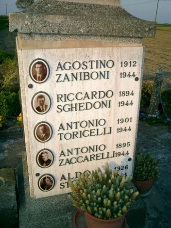 Monumento commemorativo con nomi di lavoratori coatti uccisi, incastonato in un paesaggio rurale.