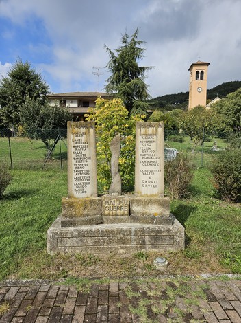 Monumento ai Caduti di Castione de' Baratti, con iscrizioni e scultura, circondato da verde e un campanile sullo sfondo.
