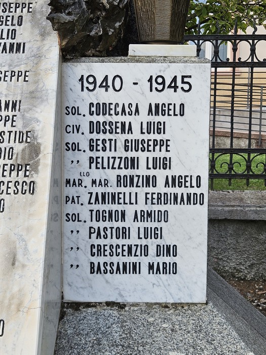 Lapide in marmo con elenco di nomi, fissata su un pilastro accanto a un cancello in ferro battuto.