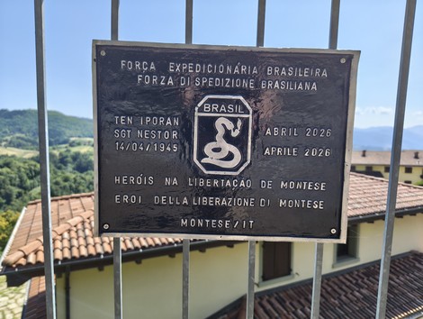 Targa commemorativa con stemma e iscrizione, fissata a una cancellata metallica davanti a un edificio.