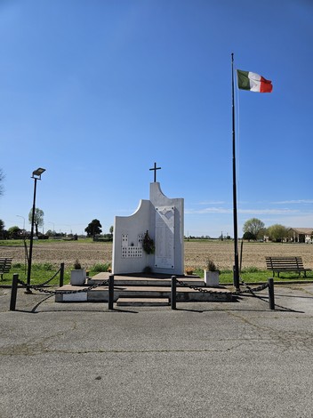Monumento ai Caduti di Valliera con bandiera italiana, situato in un'area aperta e soleggiata.
