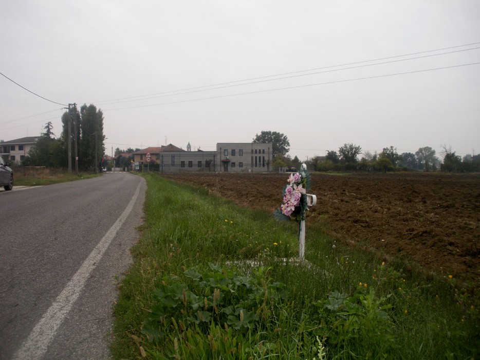 Croce a Cazzola lungo la strada, circondata da un campo e fiori, simbolo di memoria e ricordo.