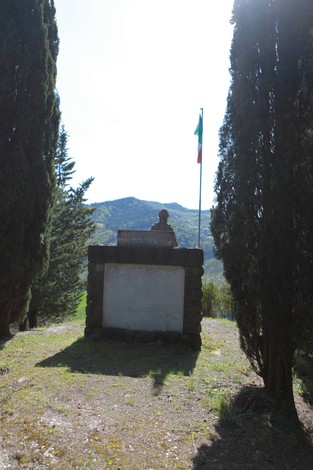 Monumento ai caduti di Purocielo, incorniciato da alberi e con vista panoramica sulle colline.